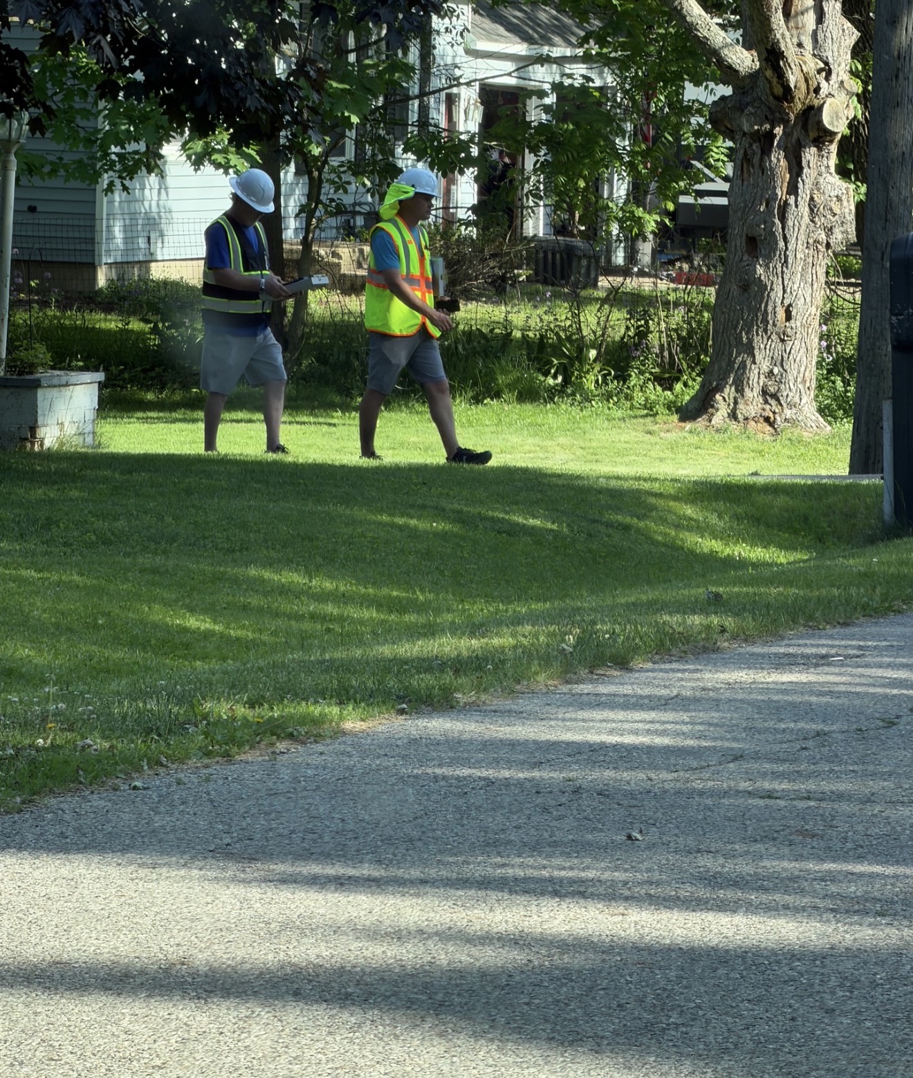 Two team members walking through a neighborhood wearing safety vests and hard hats